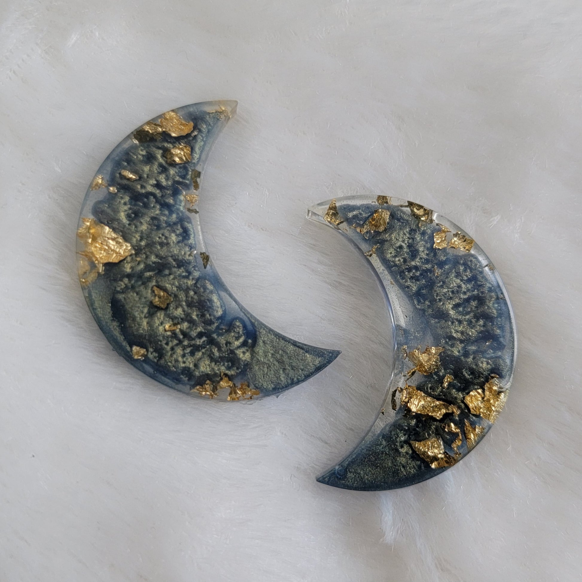 Two crescent moon shaped epoxy resin pieces with misty blue swirls and gold foil flakes.