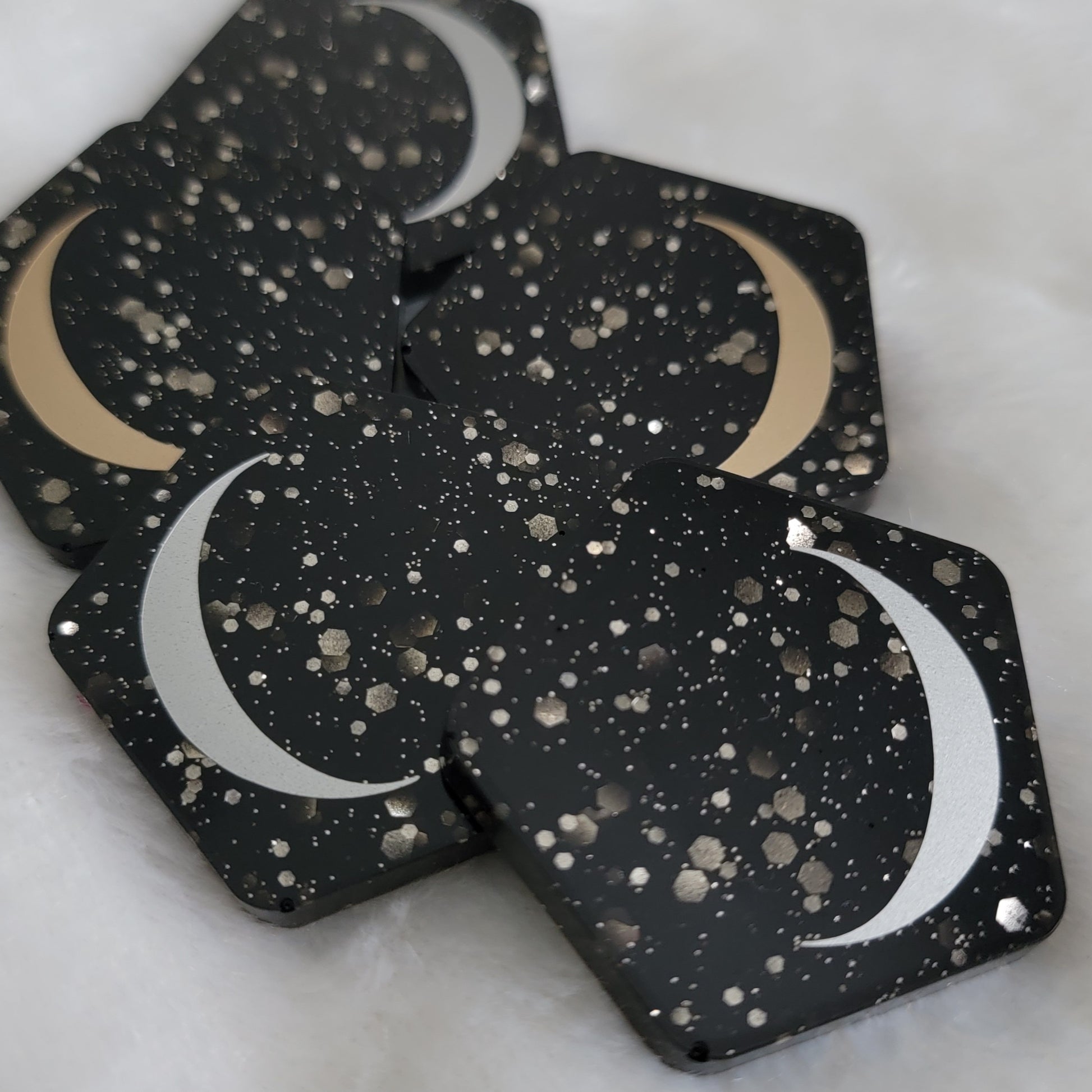 Five pentagon shaped epoxy resin pieces, black with silver glitter bases with silver and gold crescent moon motif.