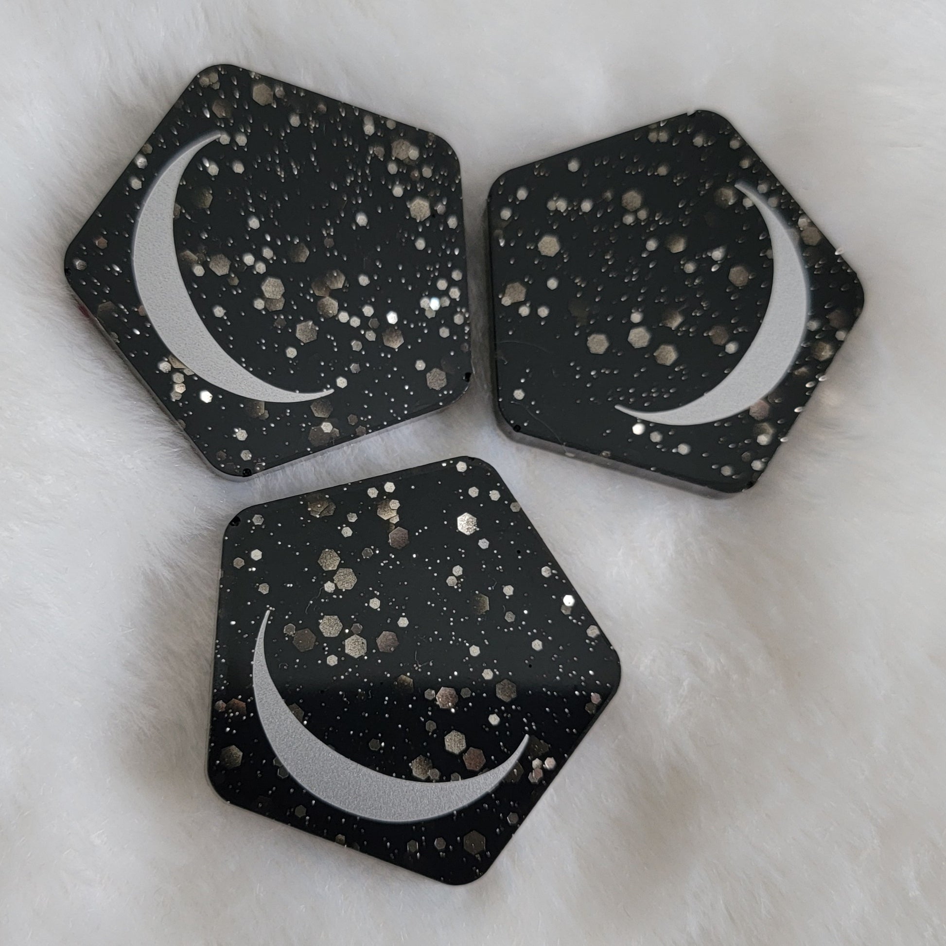 Three pentagon shaped epoxy resin pieces, black with silver glitter bases with silver crescent moon motif.