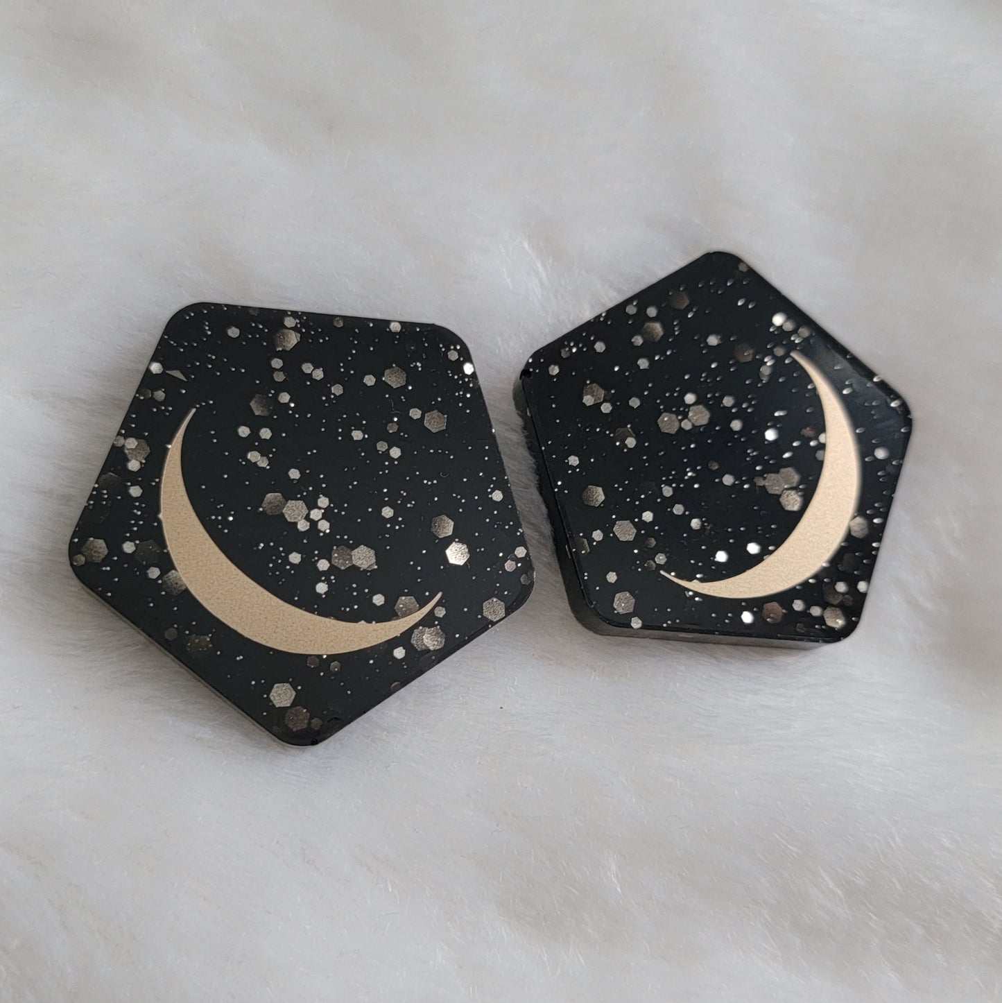 Two pentagon shaped epoxy resin pieces, black with silver glitter bases with gold crescent moon motif.