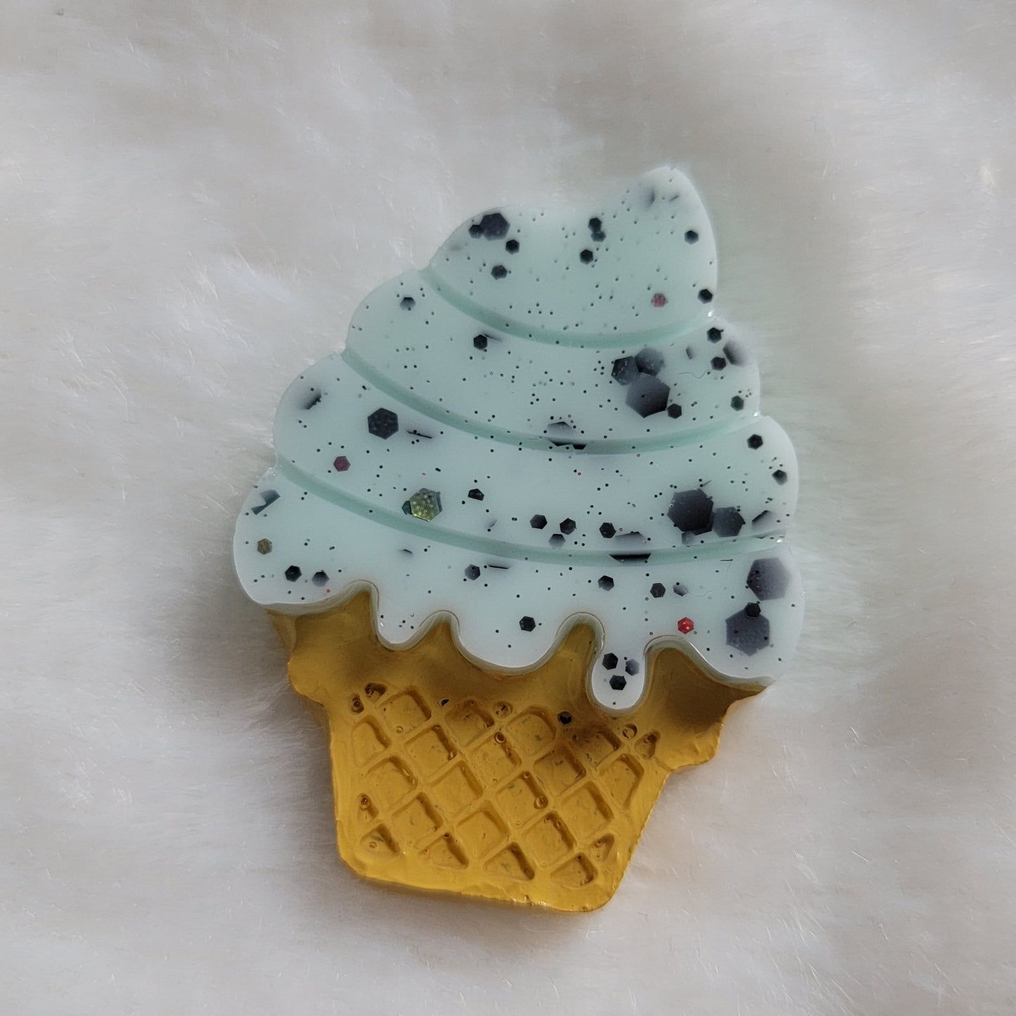 Ice cream cone shaped epoxy resin piece, light green color with black glitter mimic mint chocolate chip ice cream and cone details painted in acrylic paint.