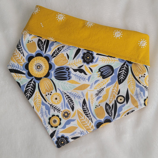 Reversible pet bandana with abstract floral print in navy, blue, aqua and mustard yellow, top edge folded down to reveal reverse side with stylized suns print on bright mustard yellow.