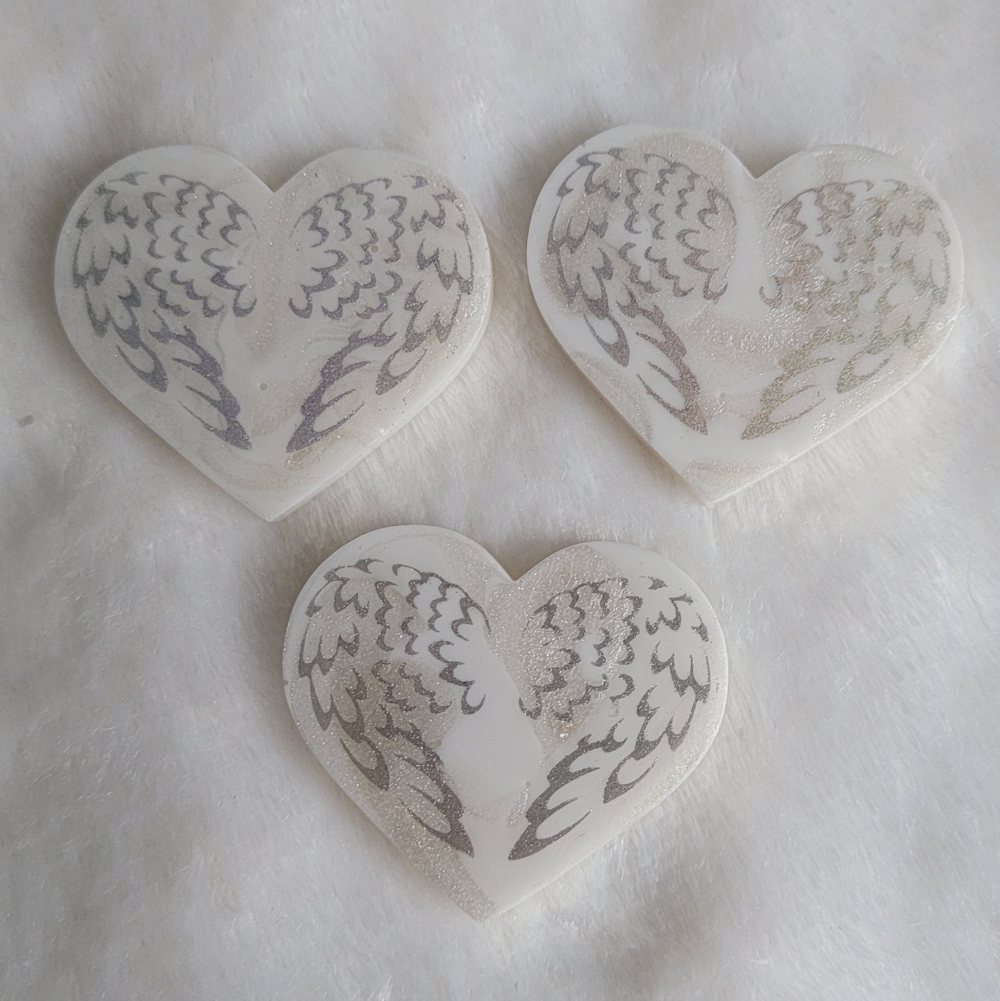 Three heart shaped resin pieces, white swirled base with silver sparkly angel wings design.