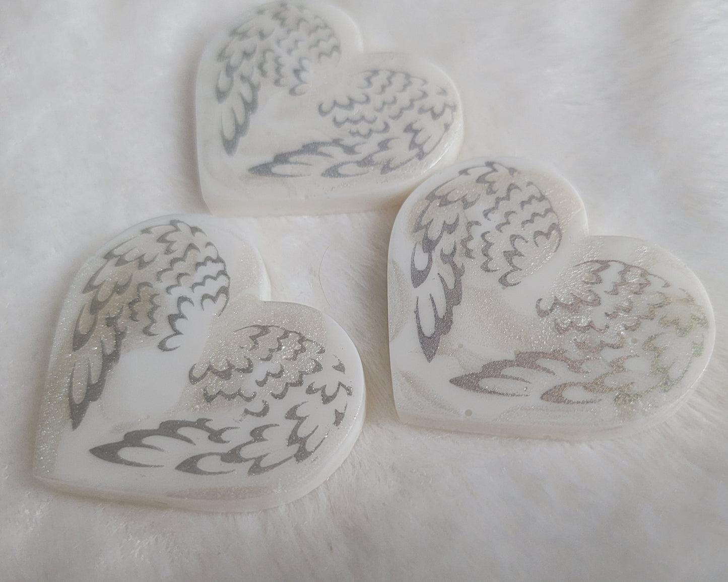 Three heart shaped resin pieces, white swirled base with silver sparkly angel wings design.