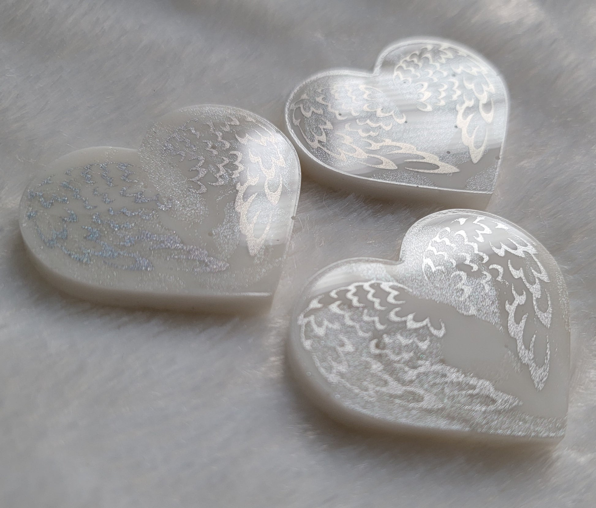 Three heart shaped resin pieces, white swirled base with silver sparkly angel wings design.