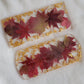 Two rectangular resin pieces, one with rounded ends, with fall leaves in shades of deep red and gold foil flakes cast in them.