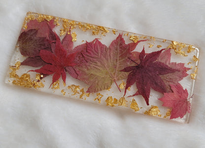 Rectangular resin piece with fall leaves in shades of deep red and gold foil flakes cast in it.