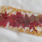 Rectangular resin piece with rounded ends, with fall leaves in shades of deep red and gold foil flakes cast in it.