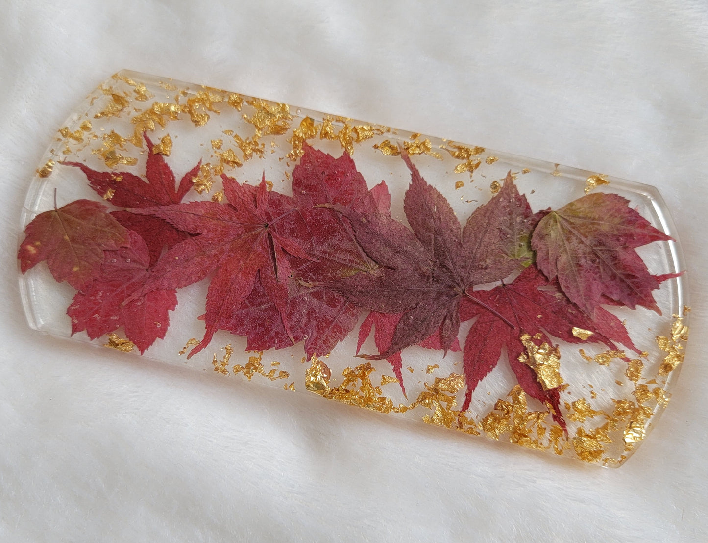 Rectangular resin piece with rounded ends, with fall leaves in shades of deep red and gold foil flakes cast in it.