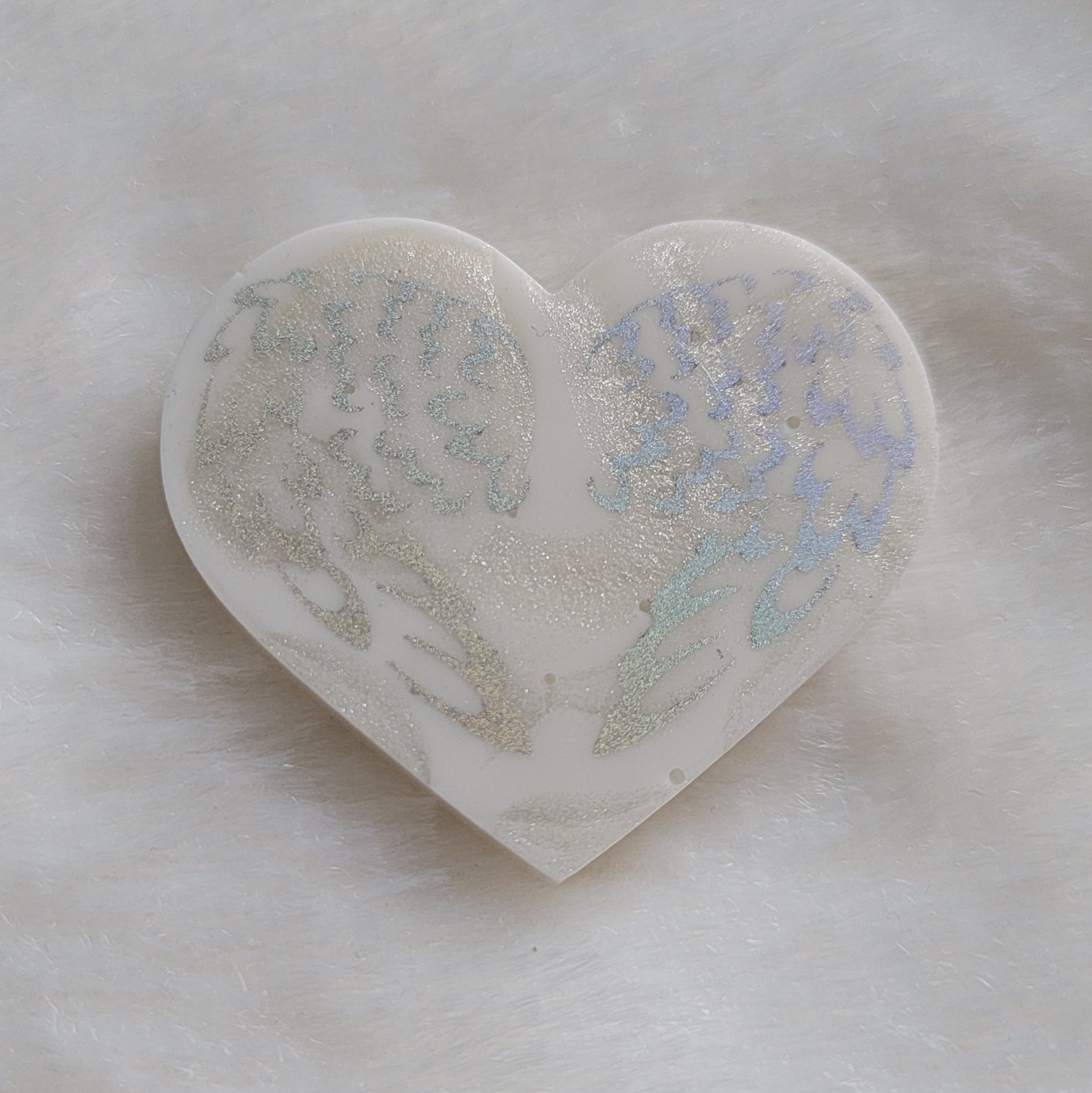 Heart shaped resin piece, white swirled base with silver holographic sparkly angel wings design.