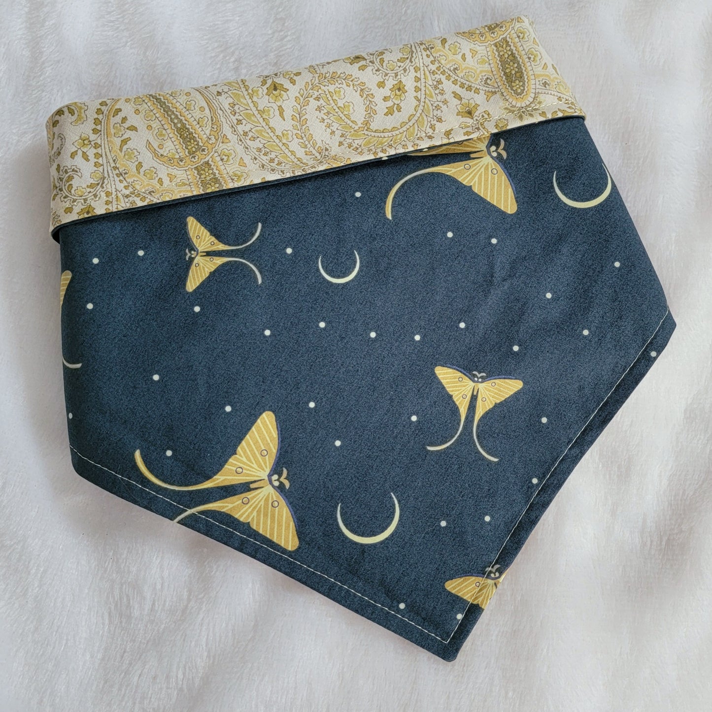 Reversible pet bandana, deep blue-green with moons and Luna moths print in soft light green, top edge folded down to show reverse side in pale paisley print.