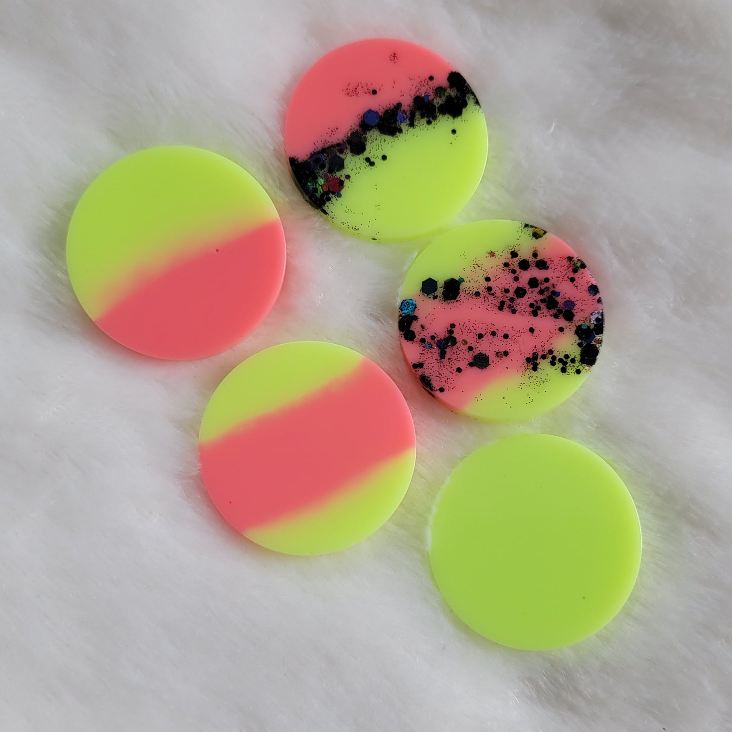 Five round epoxy resin pieces in various combinations of neon pink and neon yellow green, two with black holographic glitter.