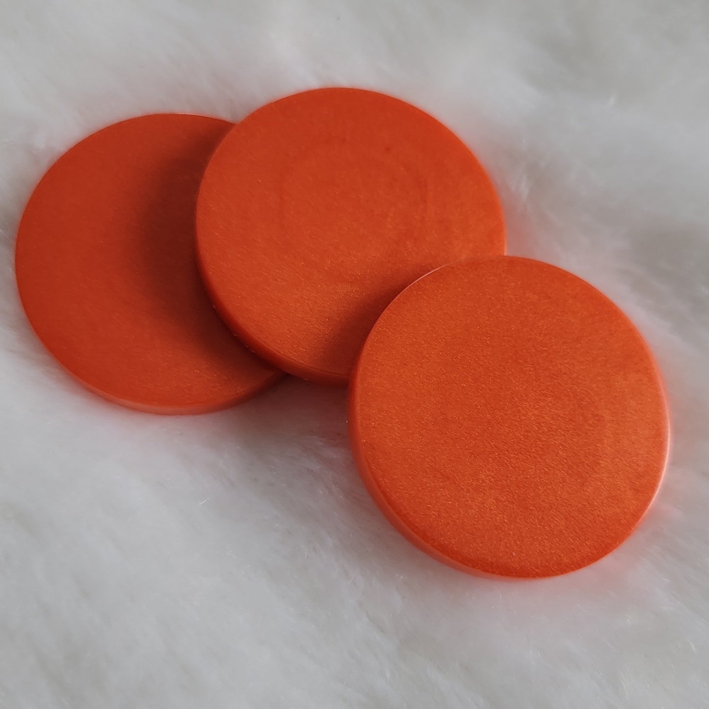 Three round epoxy resin pieces with shimmering deep orange pigment.