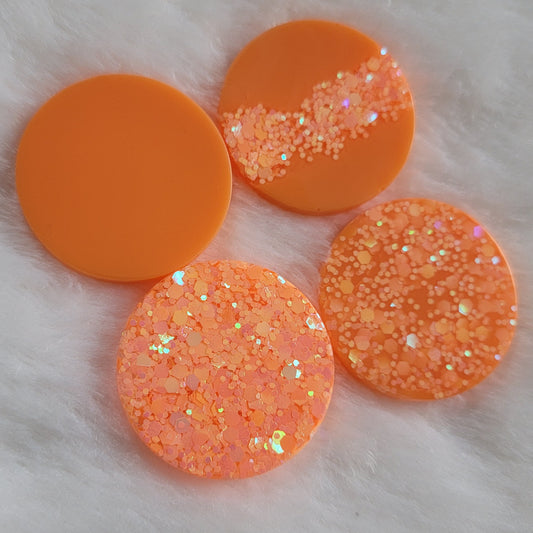 Four bright orange round epoxy resin pieces with various combinations of solid pigment and glitter.