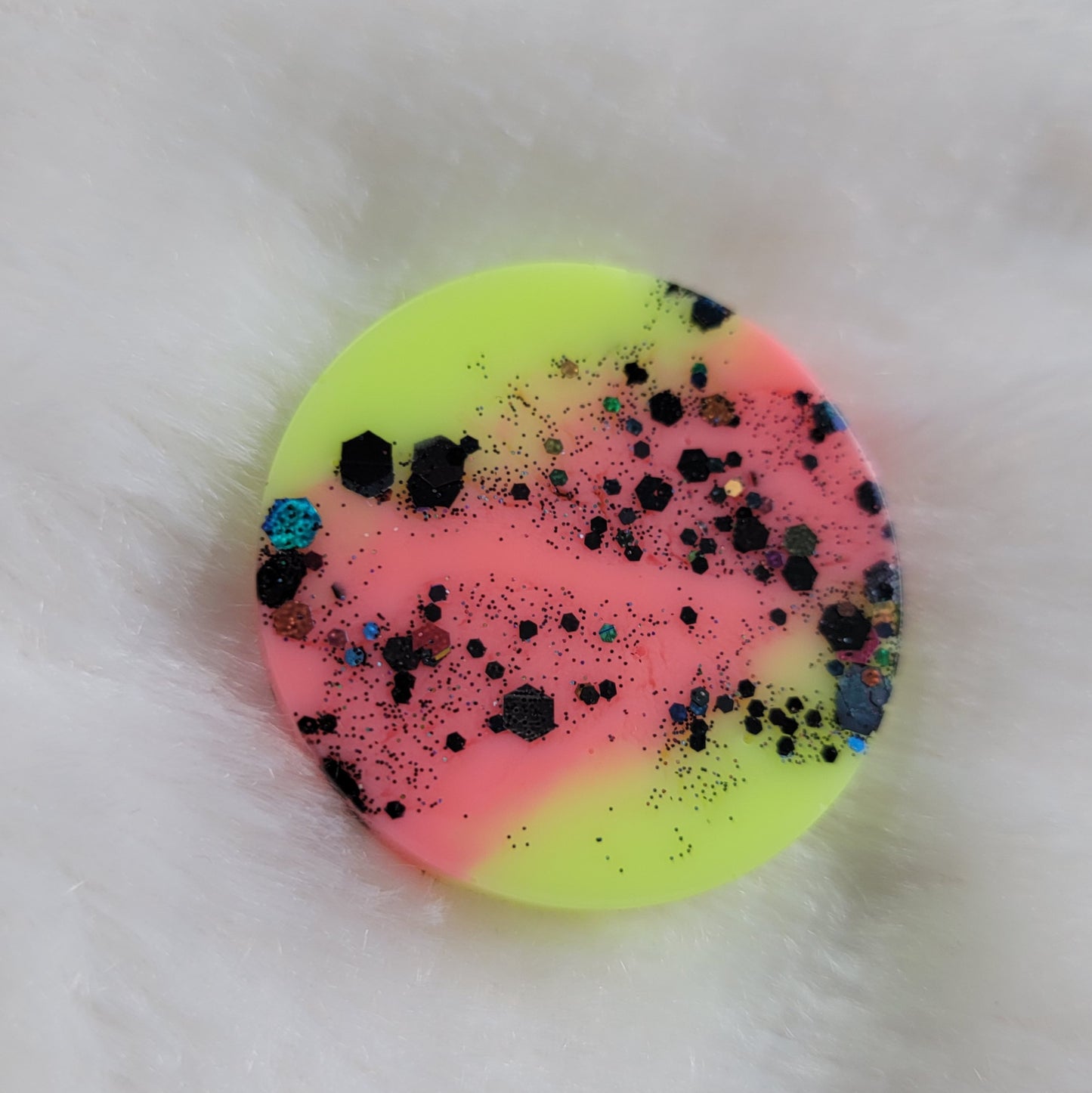 Round epoxy resin piece with neon pink stripe between neon yellow green and black holographic glitter.