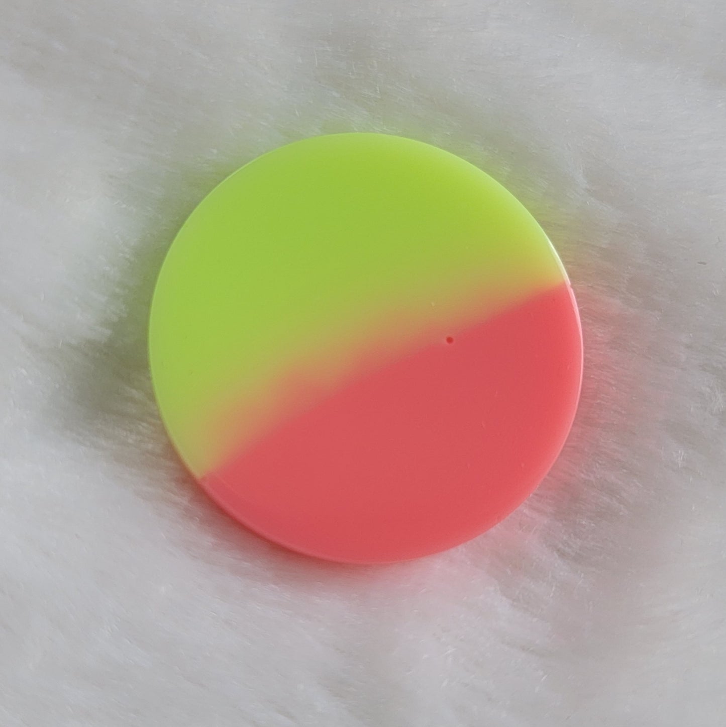 Round epoxy resin piece, half neon pink and half neon yellow-green.