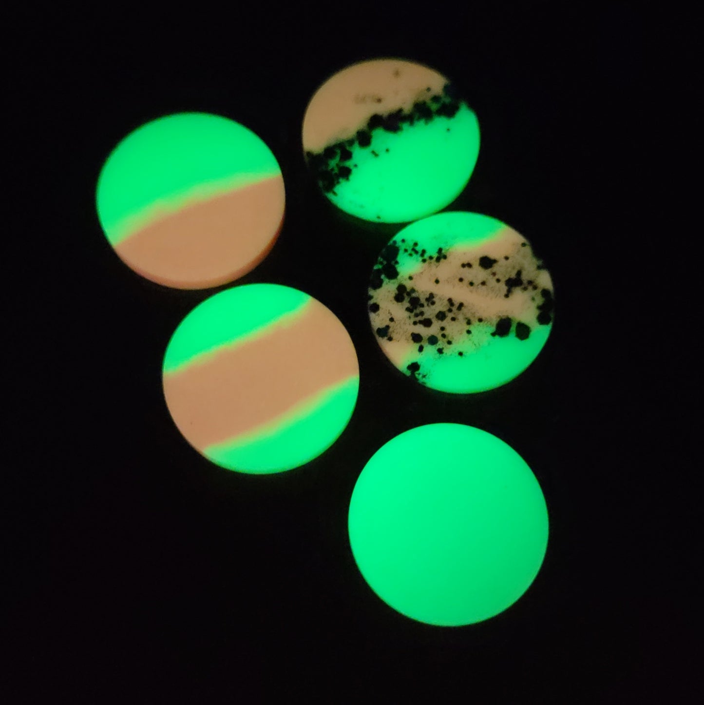 Five round epoxy resin pieces, photographed in the dark to show glow effect in lime green and coral pink.