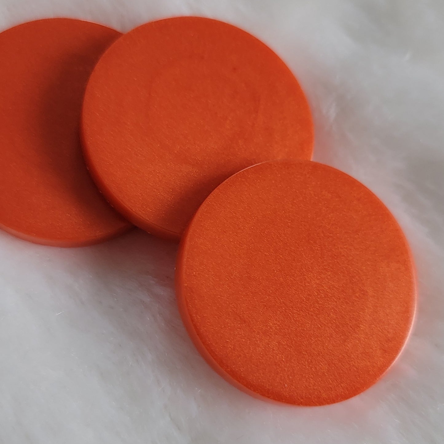 Three round epoxy resin pieces with shimmering deep orange pigment.