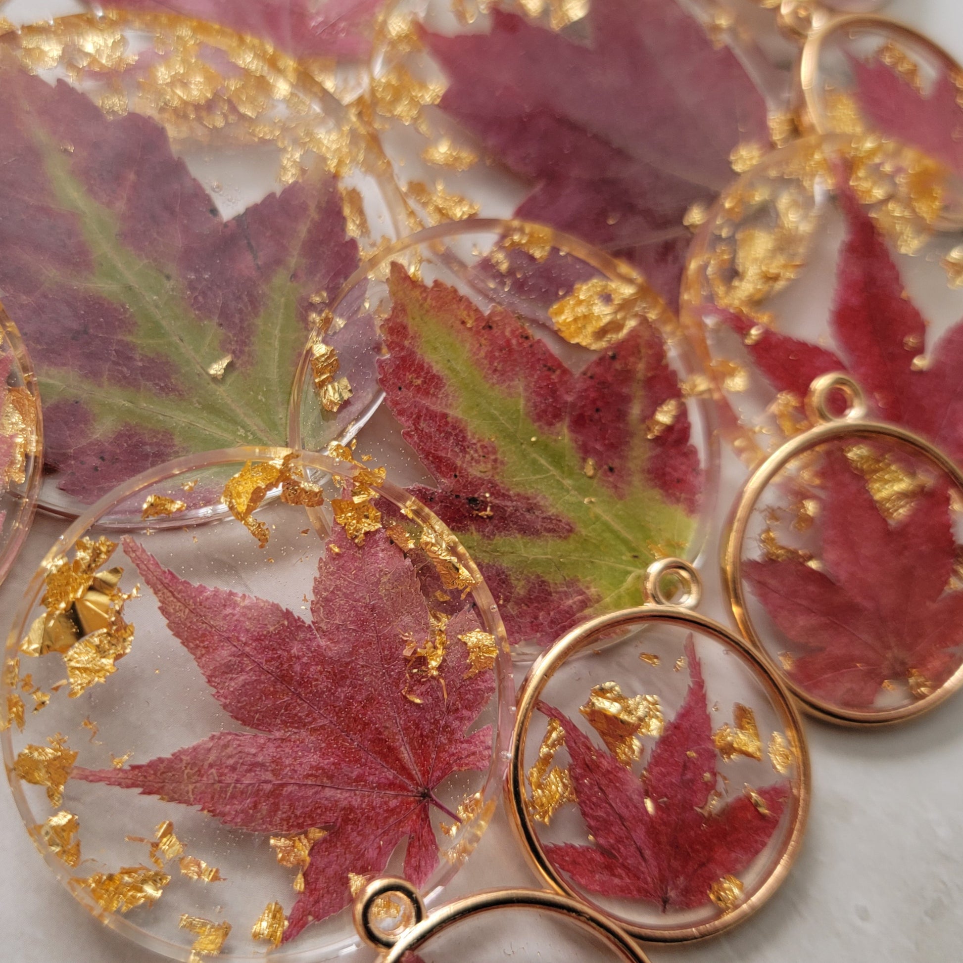 Fall leaves and gold foil flakes cast in round epoxy resin pieces, array of pieces and sizes fills the frame of picture.