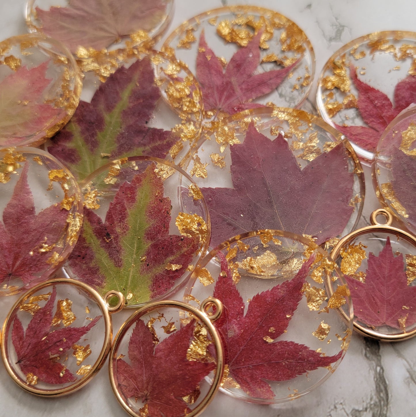 Fall leaves and gold foil flakes cast in round epoxy resin pieces, array of pieces and sizes fills the frame of picture.