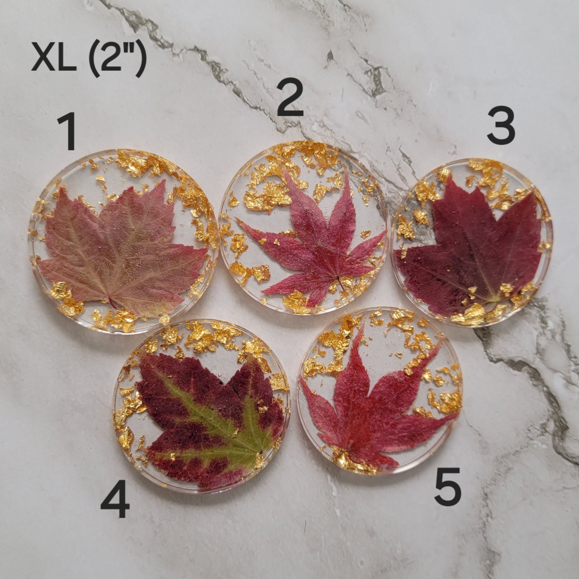 Five round epoxy resin pieces with deep red fall leaves and gold foil flakes cast in them, photo shows options for XL size.