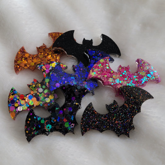 Seven small epoxy resin bats in black, purple, pink, orange, and multicolor glitter.