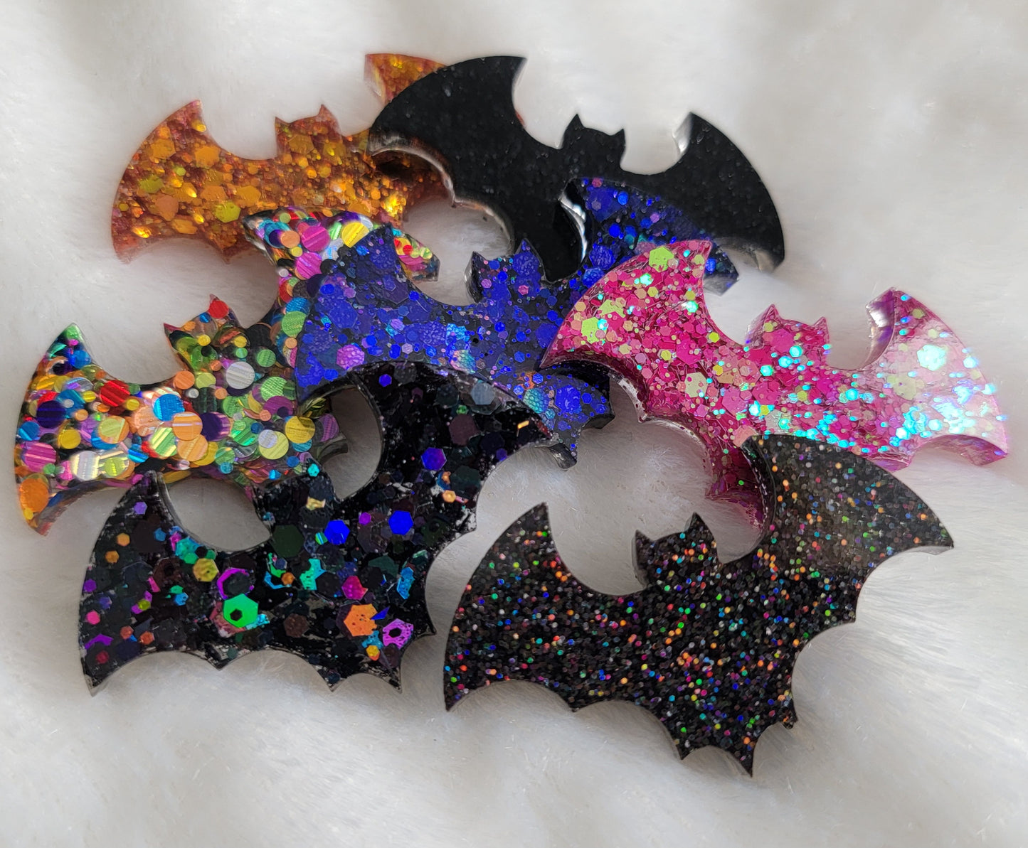 Seven small epoxy resin bats in black, purple, pink, orange, and multicolor glitter.