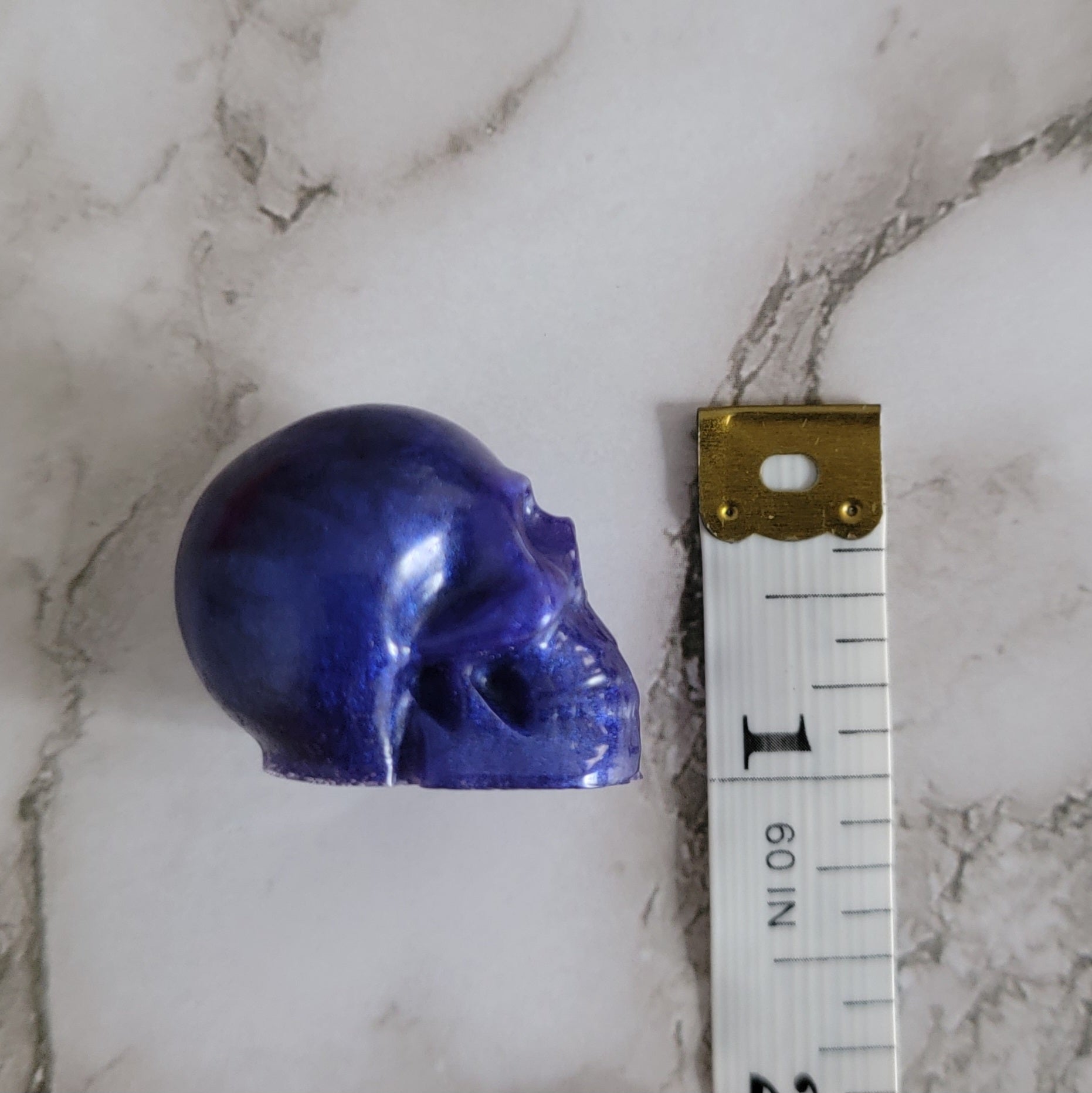 Small purple epoxy resin skull with measuring tape to show height of piece measures 1".