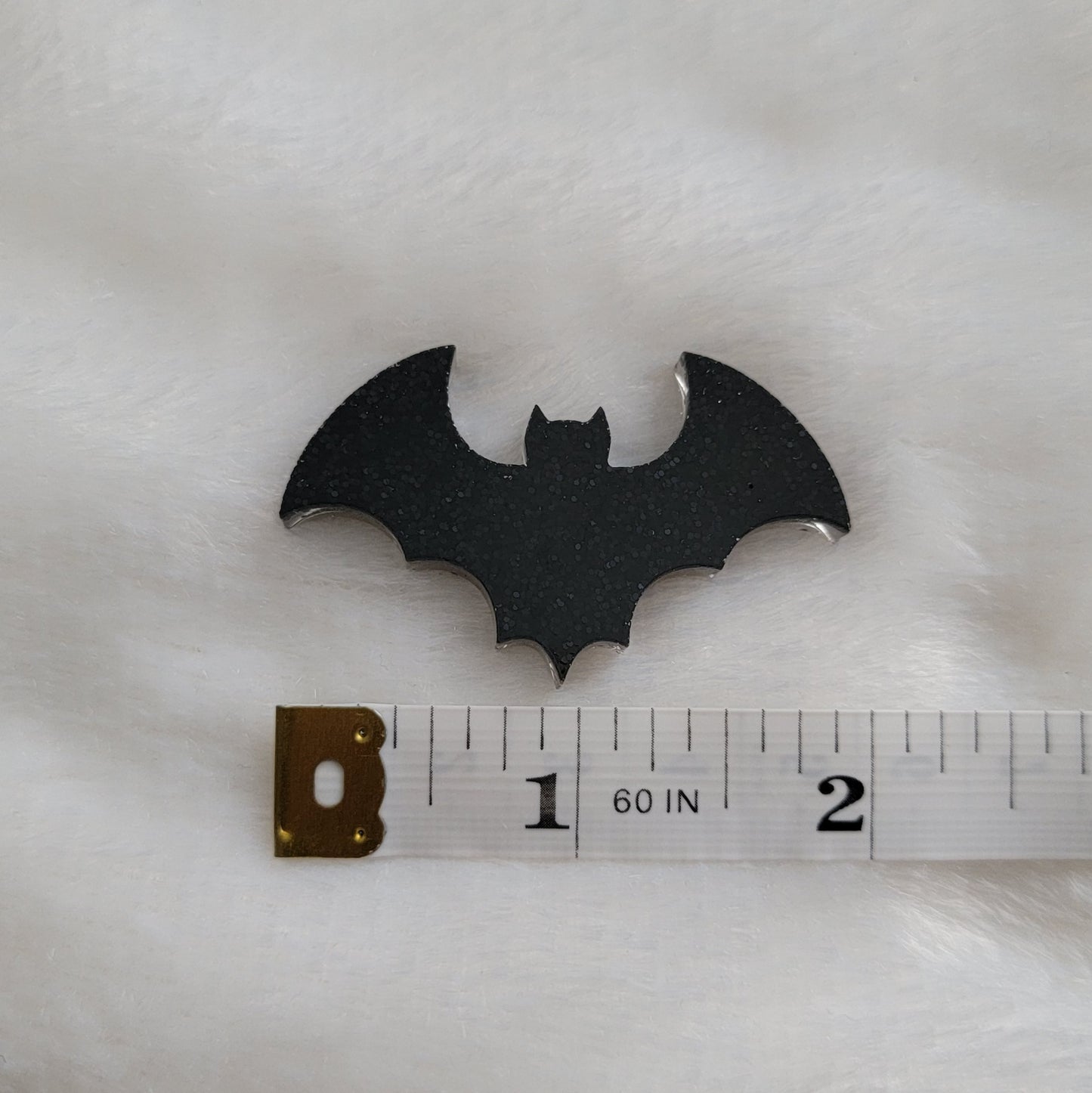 Small black glitter epoxy resin bat with measuring tape to show width of piece is 2".