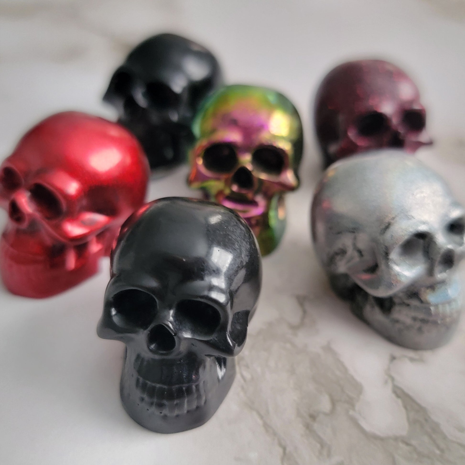 Six small epoxy resin skulls, shown in black, red, silver prism, and chameleon fuchsia.