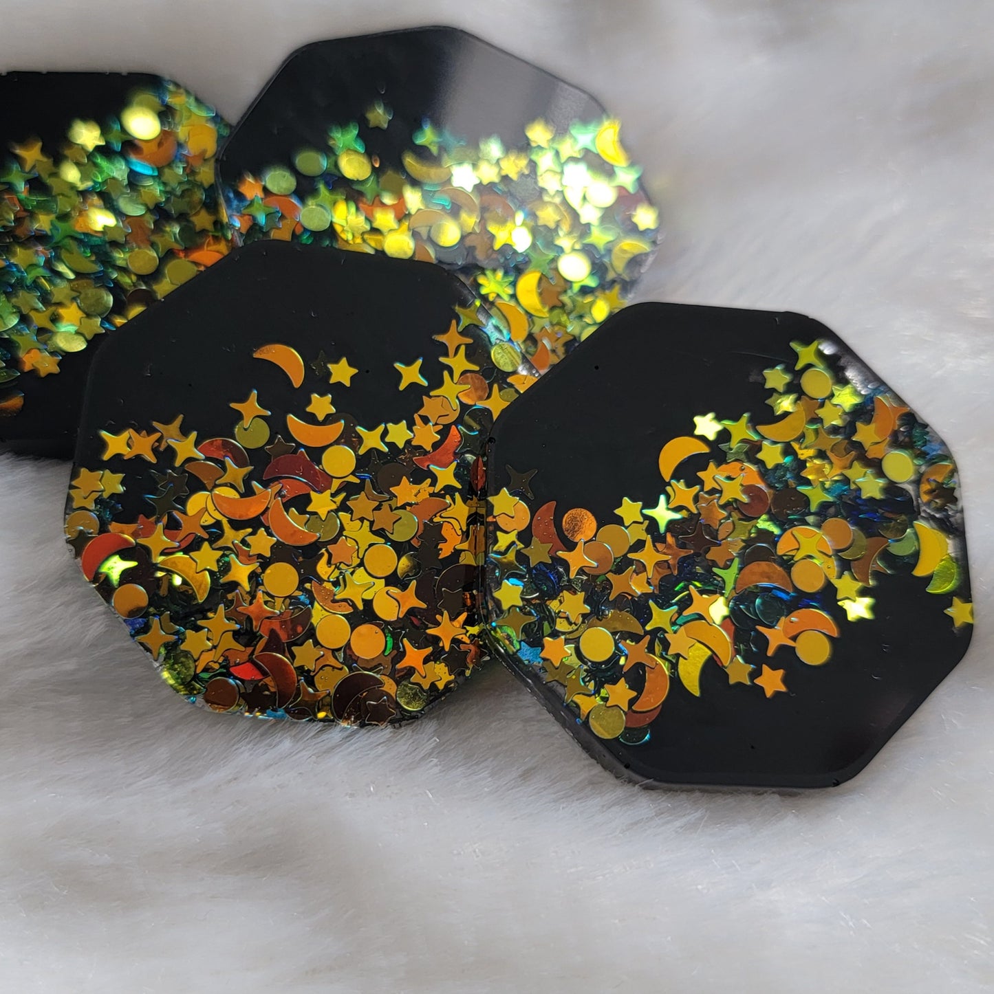 Four octagon shaped epoxy resin pieces, black with deep gold iridescent glitter in star and moon shapes.