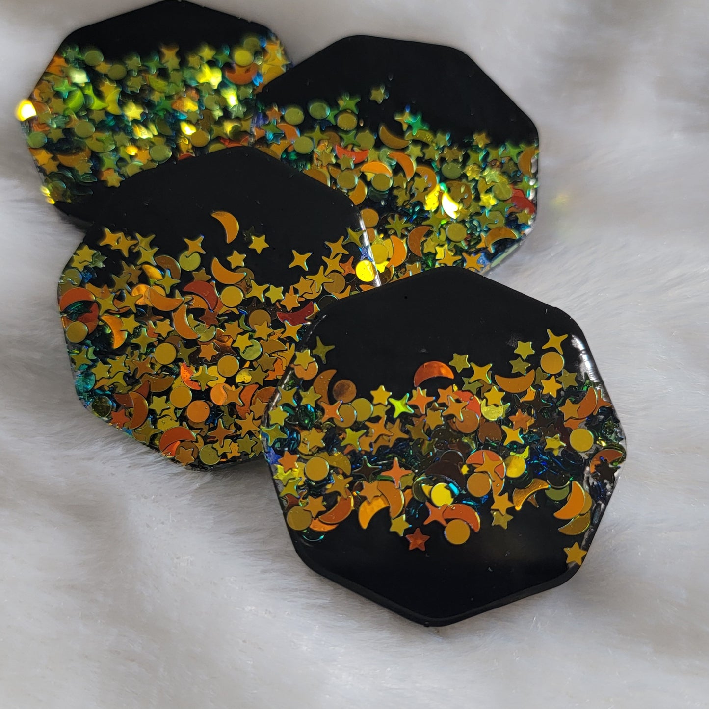 Four octagon shaped epoxy resin pieces, black with deep gold iridescent glitter in star and moon shapes.