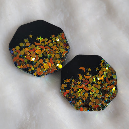 Two octagon shaped epoxy resin pieces, black with deep gold iridescent glitter in star and moon shapes.