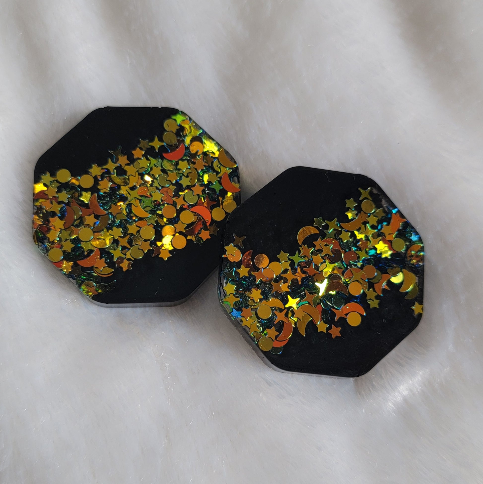 Two octagon shaped epoxy resin pieces, black with deep gold iridescent glitter in star and moon shapes.