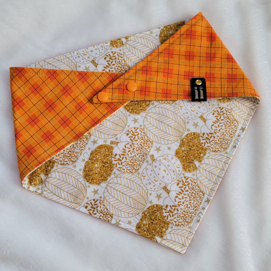 Reversible pet bandana, folded to show both sides. One side white with gold pumpkins print, other side bright orange plaid.