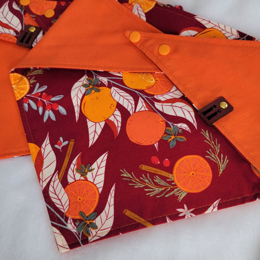 Two reversible pet bandanas, one side with burgundy citrus print and other side is bright orange, folded to show both sides of the bandanas.