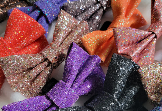 Array of several glitter bows in various fall colors including orange, purple, gold, black and red.