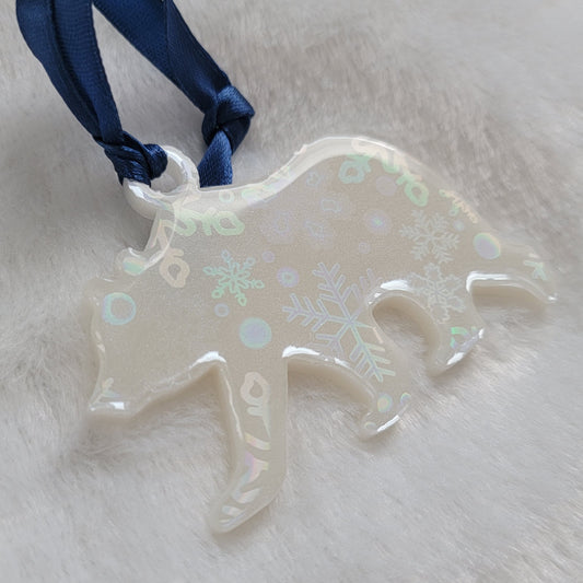 Bear shaped epoxy resin ornament, made with white pigment with a holographic snowflake print vinyl covering the entire piece and a dark blue ribbon attached.