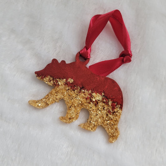 Bear shaped epoxy resin ornament, made with gold foil flakes and cherry red pigment and a red ribbon attached.