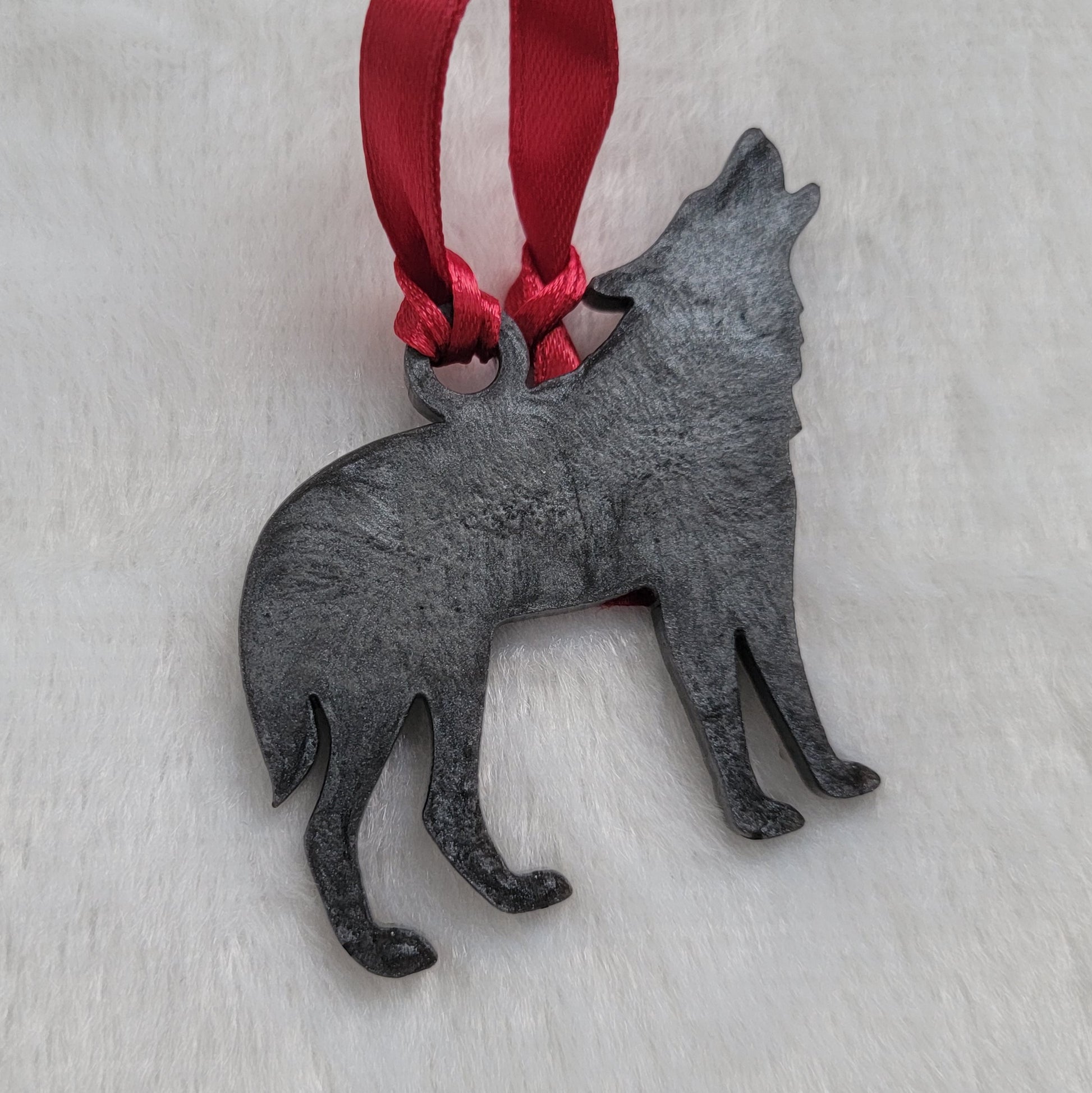 Wolf shaped epoxy resin ornament, made with dark silver pigment and a red ribbon attached.