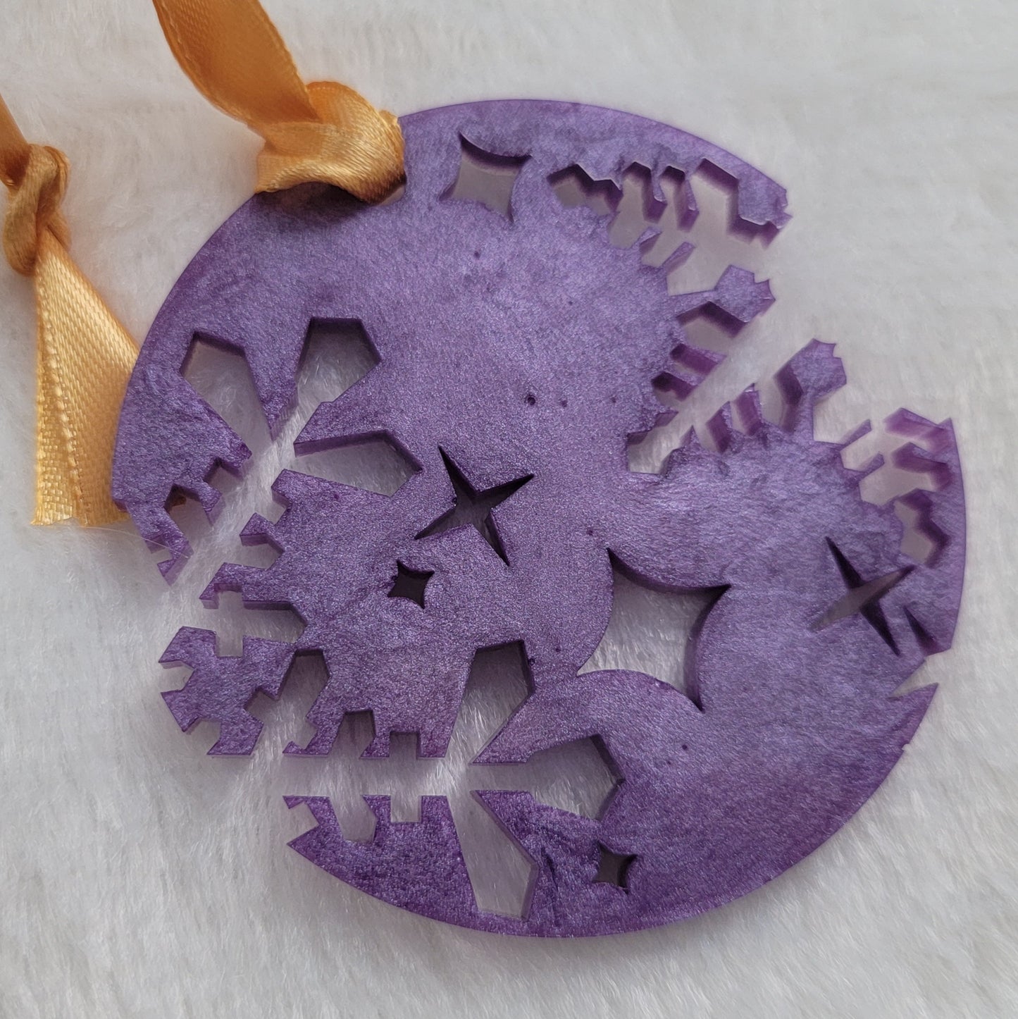 A round epoxy resin ornament that has snowflake shapes cutout from each side, made with lavender pigment and a gold ribbon attached.