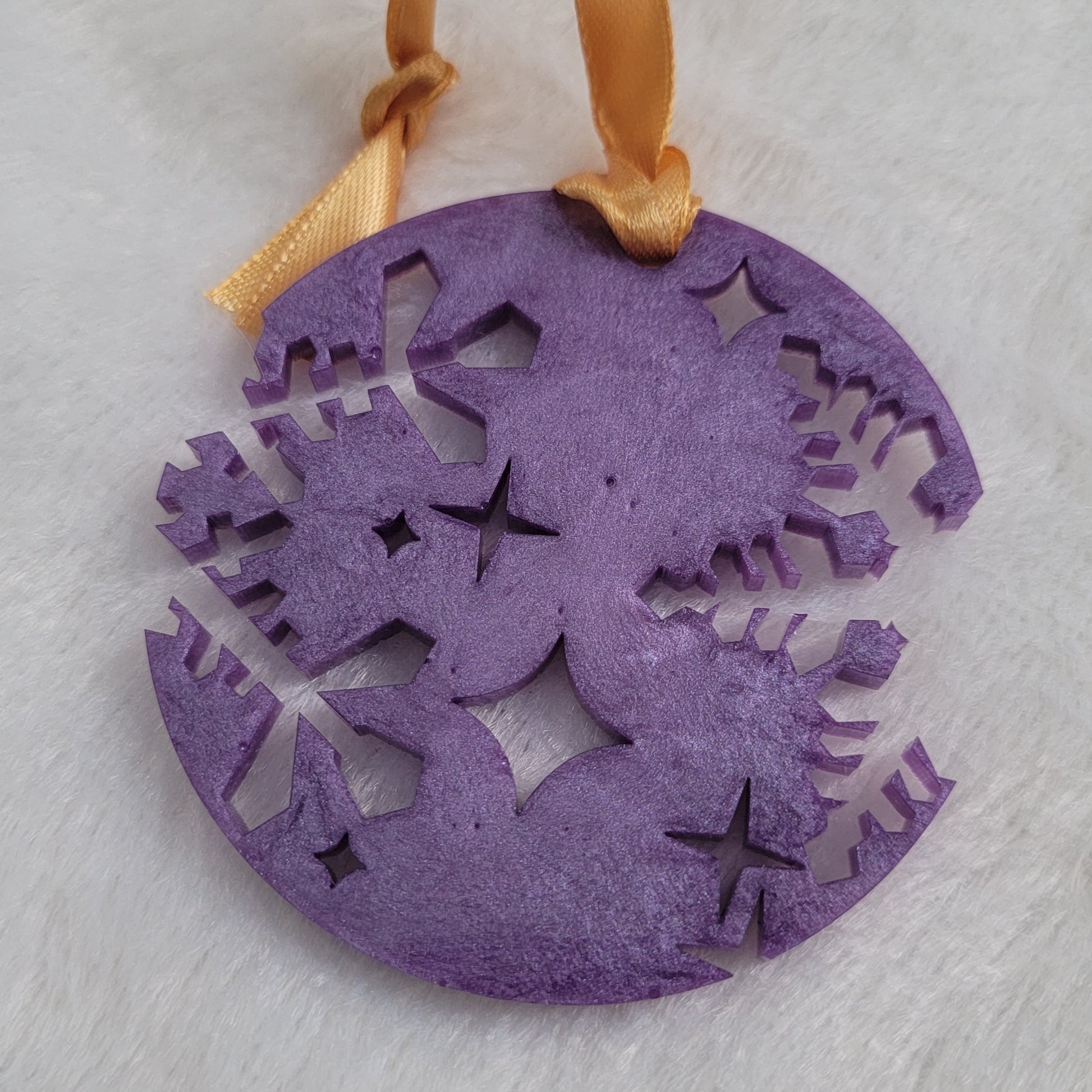 A round epoxy resin ornament that has snowflake shapes cutout from each side, made with lavender pigment and a gold ribbon attached.