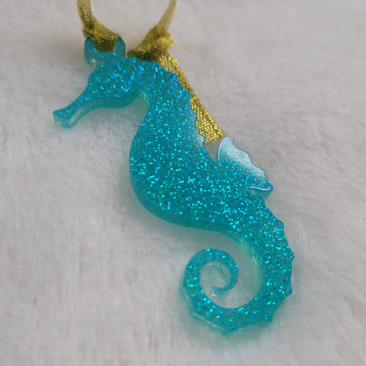 Seahorse shaped epoxy resin ornament, made with aqua glitter and a sparkling gold ribbon attached.