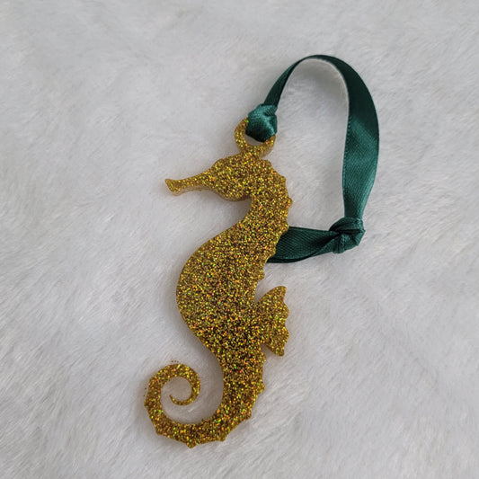 Seahorse shaped epoxy resin ornament, made with gold holographic glitter and a dark green ribbon attached.