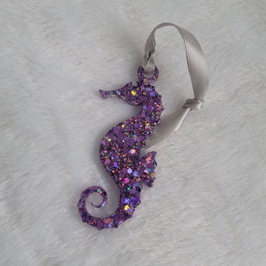 Seahorse shaped epoxy resin ornament, made with bright purple holographic glitter and a silver ribbon attached.