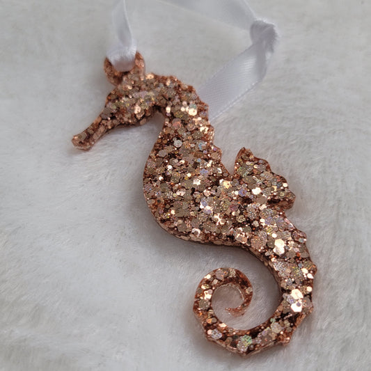 Seahorse shaped epoxy resin ornament, made with rose gold holographic glitter and a white ribbon attached.