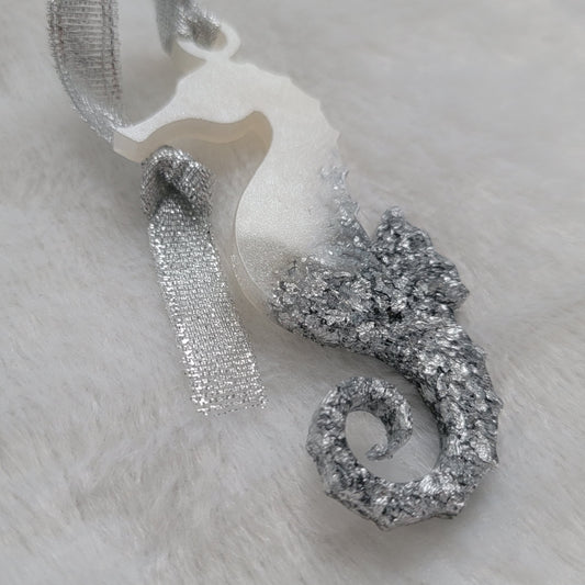 Seahorse shaped epoxy resin ornament, made with white pigment and silver foil flakes and a sparkling silver ribbon attached.