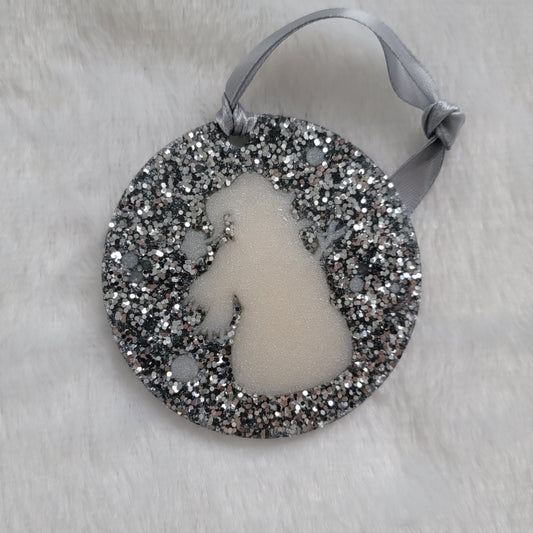 A round epoxy resin ornament that has a white snowman silhouette in the middle, made with bright silver glitter and a silver ribbon attached.