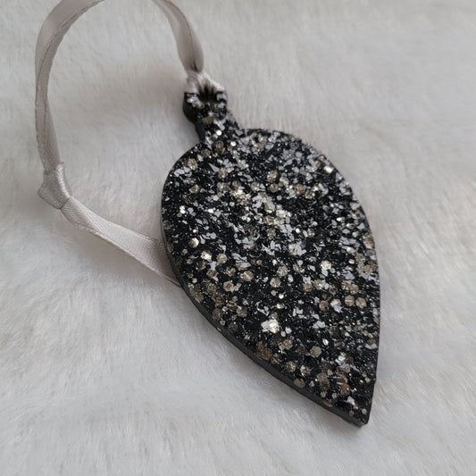 Drop shaped epoxy resin ornament that has a crystalline texture, made with black pigment and warm silver glitter combined and a silver ribbon attached.