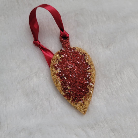 Drop shaped epoxy resin ornament that has a crystalline texture, made with gold foil flakes and cherry red pigment and a red ribbon attached.